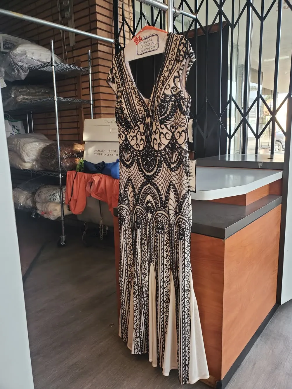 A beaded gown hanging in the shop, cleaned and ready for pickup